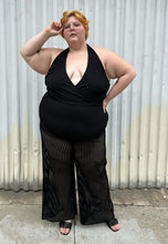 Load image into Gallery viewer, Additional full-body front view of a size 3 Fashion to Figure black halter sheer mesh vertical striped jumpsuit with a bodysuit lining styled with black heels on a size 22/24 model. The photo is taken outside in natural lighting.
