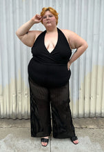 Load image into Gallery viewer, Full-body front view of a size 3 Fashion to Figure black halter sheer mesh vertical striped jumpsuit with a bodysuit lining styled with black heels on a size 22/24 model. The photo is taken outside in natural lighting.
