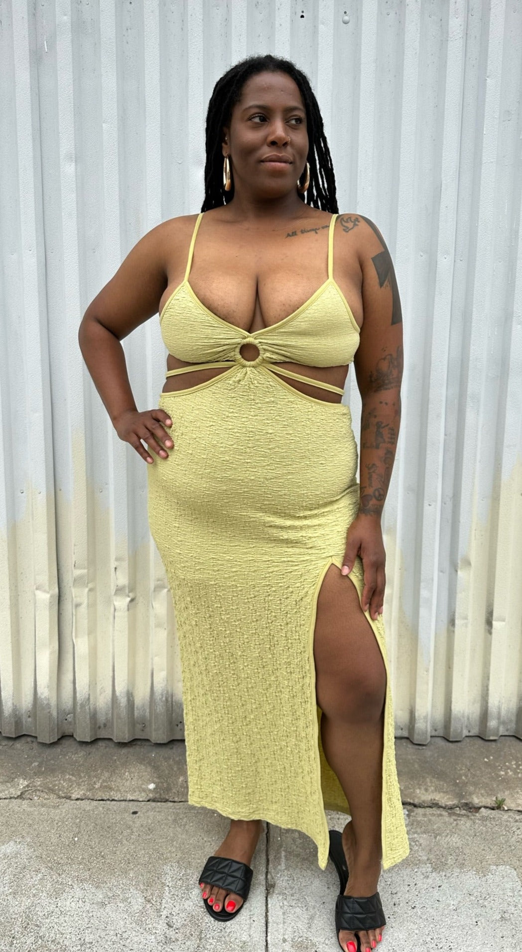 Full-body front view of a size XL Urban Outfitters chartreuse textured cut-out maxi dress with a side slit styled with black sides on a size 14/16 model. The photo is taken outside in natural lighting.