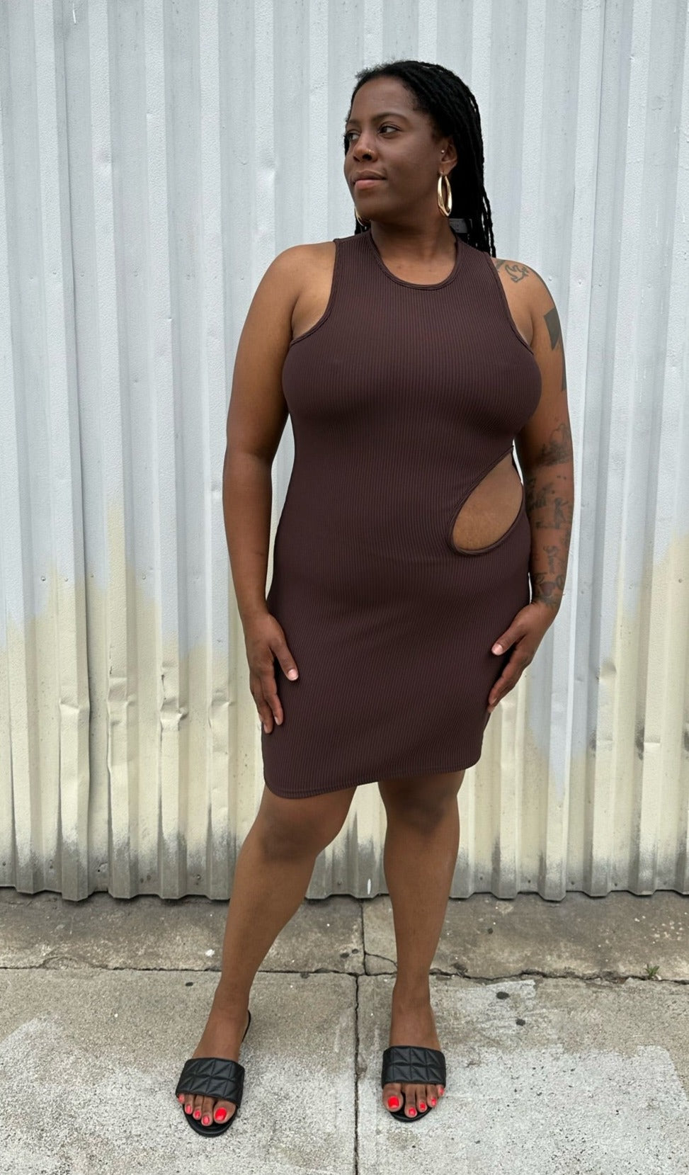 Full-body front view of a size 14 Pretty Little Thing dark brown ribbed cut-out mini bodycon dress styled with black slides on a size 14/16 model. The photo is taken outside in natural lighting.