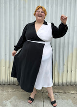 Load image into Gallery viewer, Full-body front view of a size 22 Eloquii black and white collared wrap dress styled with black slides on a size 22/24 model. The photo is taken outside in natural lighting.
