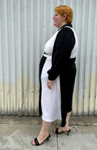 Load image into Gallery viewer, Full-body side view of a size 22 Eloquii black and white collared wrap dress styled with black slides on a size 22/24 model. The photo is taken outside in natural lighting.
