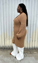 Load image into Gallery viewer, Full-body side view of a size 14/16 Eloquii light brown knit longline cardigan with subtle puff sleeves styled over white pants on a size 14/16 model. The photo is taken outside in natural lighting.
