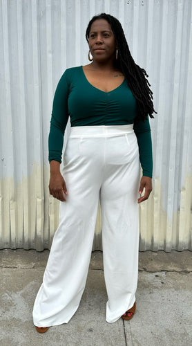 Full-body front view of a pair of size 16 Boohoo white wide leg trousers styled with a dark teal long sleeve tee on a size 14/16 model. The photo is taken outside in natural lighting.