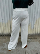 Load image into Gallery viewer, Front view of a pair of size 16 Boohoo white wide leg trousers styled with a dark teal long sleeve tee on a size 14/16 model. The photo is taken outside in natural lighting.
