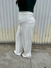 Load image into Gallery viewer, Side view of a pair of size 16 Boohoo white wide leg trousers styled with a dark teal long sleeve tee on a size 14/16 model. The photo is taken outside in natural lighting.
