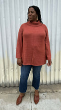 Load image into Gallery viewer, Full-body front view of a size 14/16 Eloquii dark peach longline knit turtleneck sweater with side slits styled with medium wash denim on a size 14/16 model. The photo is taken outside in natural lighting.
