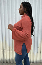 Load image into Gallery viewer, Side view of a size 14/16 Eloquii dark peach longline knit turtleneck sweater with side slits styled with medium wash denim on a size 14/16 model. The photo is taken outside in natural lighting.
