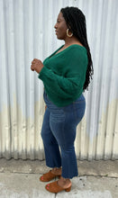 Load image into Gallery viewer, Full-body side view of a size 14/16 Eloquii emerald green twist-front cropped sweater with tummy cut-out styled with medium wash denim on a size 14/16 model. The photo is taken outside in natural lighting.
