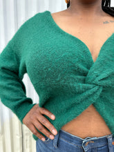 Load image into Gallery viewer, Closer front view of a size 14/16 Eloquii emerald green twist-front cropped sweater with tummy cut-out styled with medium wash denim on a size 14/16 model. The photo is taken outside in natural lighting.
