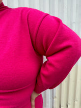 Load image into Gallery viewer, Close view of the sweater material on the sleeve of a size 22/24 Eloquii hot pink sweater dress with turtleneck top, keyhole bust, and belly cut-out on a size 22/24 model. The photo is taken outside in natural lighting.
