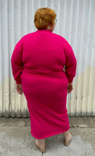 Load image into Gallery viewer, Full-body back view of a size 22/24 Eloquii hot pink sweater dress with turtleneck top, keyhole bust, and belly cut-out styled with gold flats on a size 22/24 model. The photo is taken outside in natural lighting.
