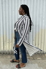 Load image into Gallery viewer, Full-body side view of a size 18 Pink Clove black and white vertical striped collared duster styled open over a white tee, dark jeans, and black slides on a size 14/16 model. The photo is taken outside in natural lighting.
