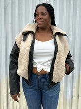 Load image into Gallery viewer, Front view of a size XXL Rachel Parcell black and ivory shearling zip-up bomber jacket styled unzipped over a white tied-up tee and medium wash denim on a size 14/16 model. The photo was taken outside in natural lighting.
