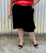 Load image into Gallery viewer, Front view of a size 26 Lane Bryant black handkerchief hem midi skirt with zipper closure styled with a red pleather sleeveless crop top and black kitten heels on a size 22/24 model. The photo is taken outside in natural lighting.
