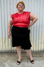 Load image into Gallery viewer, Full-body front view of a size 26 Lane Bryant black handkerchief hem midi skirt with zipper closure styled with a red pleather sleeveless crop top and black kitten heels on a size 22/24 model. The photo is taken outside in natural lighting.
