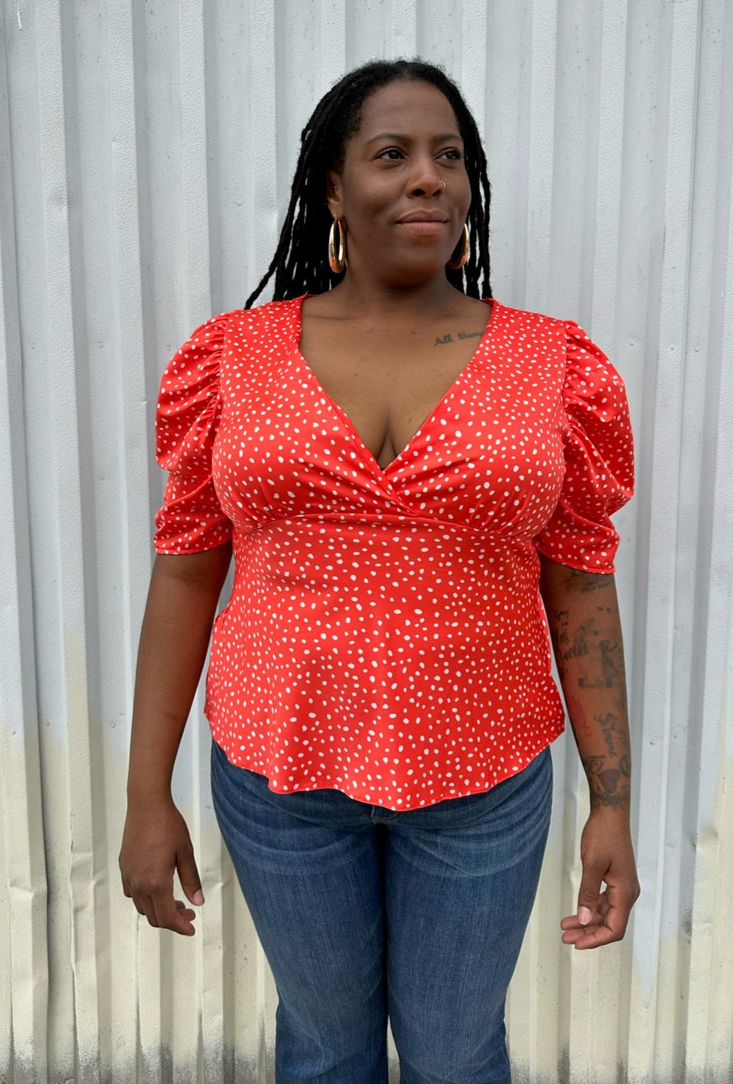Front view of a size 14 ASOS bright red and white polka dot v-neck puff sleeve blouse styled with medium wash denim on a size 14/16 model. The photo is taken outside in natural lighting.