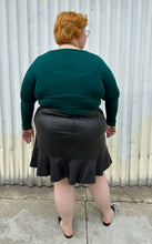 Load image into Gallery viewer, Full-body back view of a size 24 Eloquii black pleather skirt with ruffle hem styled with a teal long sleeve shirt and black slides on a size 22/24 model. The photo is taken outside in natural lighting.
