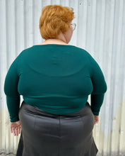 Load image into Gallery viewer, Back view of a size 18/20 Eloquii dark teal long sleeve t-shirt styled over a black pleather mini skirt on a size 22/24 model. The photo is taken outside in natural lighting.
