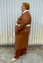 Load image into Gallery viewer, Full-body side view of a size 22/24 Eloquii light brown, dark brown, and cream pleather collared trench coat with contrast colors and belt styled buttoned up and belted over a brown sheer shirt, rust silky pants, and gold flats on a size 22/24 model. The photo is taken outside in natural lighting.
