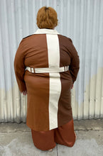 Load image into Gallery viewer, Full-body back view of a size 22/24 Eloquii light brown, dark brown, and cream pleather collared trench coat with contrast colors and belt styled buttoned up and belted over a brown sheer shirt, rust silky pants, and gold flats on a size 22/24 model. The photo is taken outside in natural lighting.
