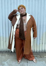Load image into Gallery viewer, Full-body front view of a size 22/24 Eloquii light brown, dark brown, and cream pleather collared trench coat with contrast colors and belt styled unbuttoned, open over a brown sheer shirt, rust silky pants, and gold flats on a size 22/24 model. The photo is taken outside in natural lighting.
