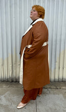 Load image into Gallery viewer, Full-body side view of a size 22/24 Eloquii light brown, dark brown, and cream pleather collared trench coat with contrast colors and belt styled unbuttoned, open over a brown sheer shirt, rust silky pants, and gold flats on a size 22/24 model. The photo is taken outside in natural lighting.
