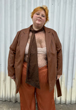 Load image into Gallery viewer, Front view of a size 22 Eloquii warm tone brown belted pleather blazer jacket styled open over a dark brown sheer shirt and rust silky pants on a size 22/24 model. The photo is taken outside in natural lighting.
