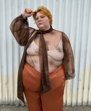 Load image into Gallery viewer, Front view showing off the sleeve of a size 22/24 Eloquii dark brown sheer puff sleeve pussybow blouse styled tucked into a pair of rust colored silky pants on a size 22/24 model. The photo is taken outside in natural lighting.
