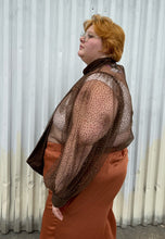 Load image into Gallery viewer, Side view of a size 22/24 Eloquii dark brown sheer puff sleeve pussybow blouse styled tucked into a pair of rust colored silky pants on a size 22/24 model. The photo is taken outside in natural lighting.

