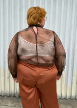 Load image into Gallery viewer, Back view of a size 22/24 Eloquii dark brown sheer puff sleeve pussybow blouse styled tucked into a pair of rust colored silky pants on a size 22/24 model. The photo is taken outside in natural lighting.
