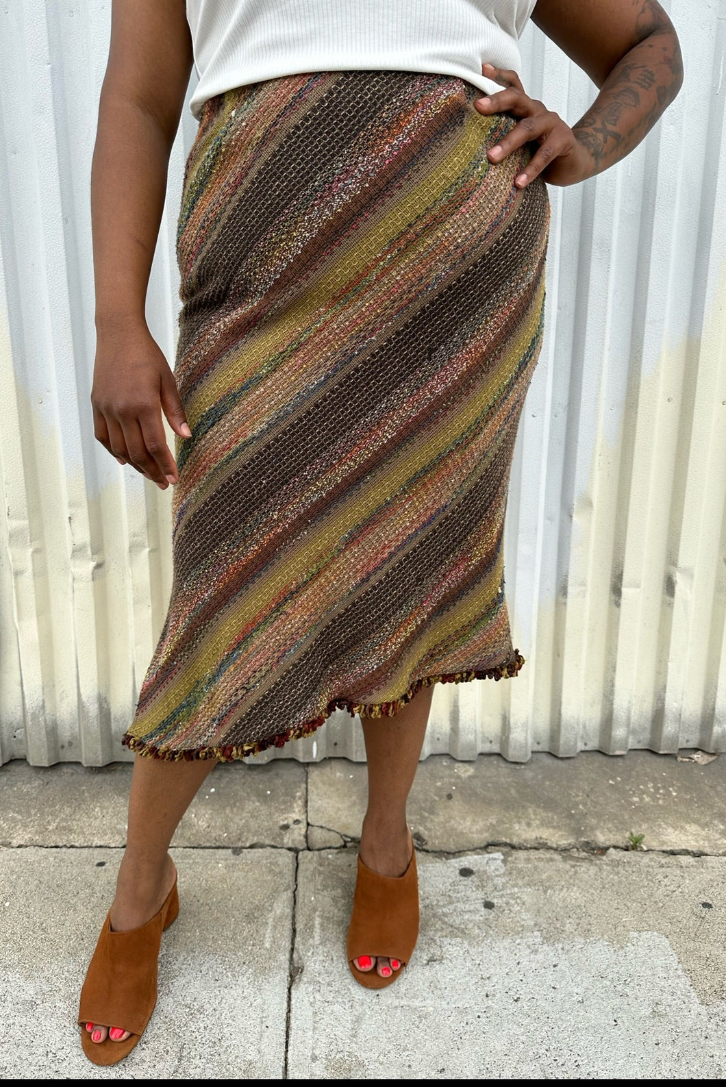 Front view of a size 14 Nancy Bolen City Girl vintage earth tone horizonatl striped midi skirt styled with a ribbed whit tank and warm tone brown mules on a size 14 model. The photo is taken outside in natural lighting.