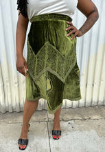 Load image into Gallery viewer, Front view of a size 12/14 Vestiaire Collective forest green crushed velvet handkerchief hem midi skirt with mixed materials woven and embroidered in styled with a white top and black kitten heels on a size 14/16 model. The photo is taken outside in natural lighting.
