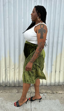 Load image into Gallery viewer, Full-body side view of a size 12/14 Vestiaire Collective forest green crushed velvet handkerchief hem midi skirt with mixed materials woven and embroidered in styled with a white top and black kitten heels on a size 14/16 model. The photo is taken outside in natural lighting.
