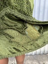 Load image into Gallery viewer, Additional close up view of the embroidered and woven textured details of a size 12/14 Vestiaire Collective forest green crushed velvet handkerchief hem midi skirt with mixed materials woven and embroidered in on a size 14/16 model. The photo is taken outside in natural lighting.
