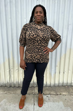 Load image into Gallery viewer, Full-body front view of a size XXL Halogen leopard pattern three-quarter length sleeve turtleneck sweater styled with black pants and brown mules on a size 14/16 model. The photo is taken outside in natural lighting. 
