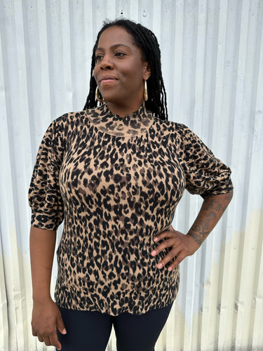 Front view of a size XXL Halogen leopard pattern three-quarter length sleeve turtleneck sweater styled with black pants on a size 14/16 model. The photo is taken outside in natural lighting. 