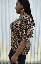 Load image into Gallery viewer, Side view of a size XXL Halogen leopard pattern three-quarter length sleeve turtleneck sweater styled with black pants on a size 14/16 model. The photo is taken outside in natural lighting. 

