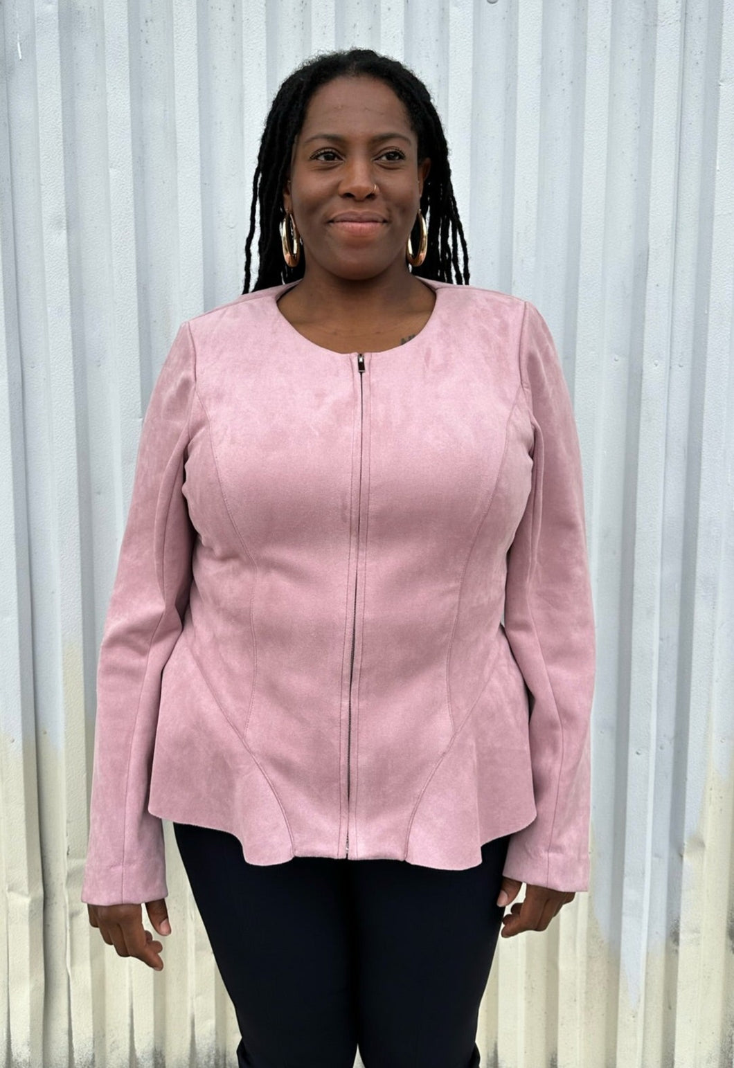 Front view of a size 16 Lane Bryant baby pink suede zip-up corset-back jacket styled over black pants on a size 14/16 model. The photo is taken outside in natural lighting.