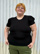 Load image into Gallery viewer, Front view of a size 3X Forever 21 black subtle puff sleeve t-shirt styled over green cargo pants on a size 22/24 model. The photo is taken outside in natural lighting.
