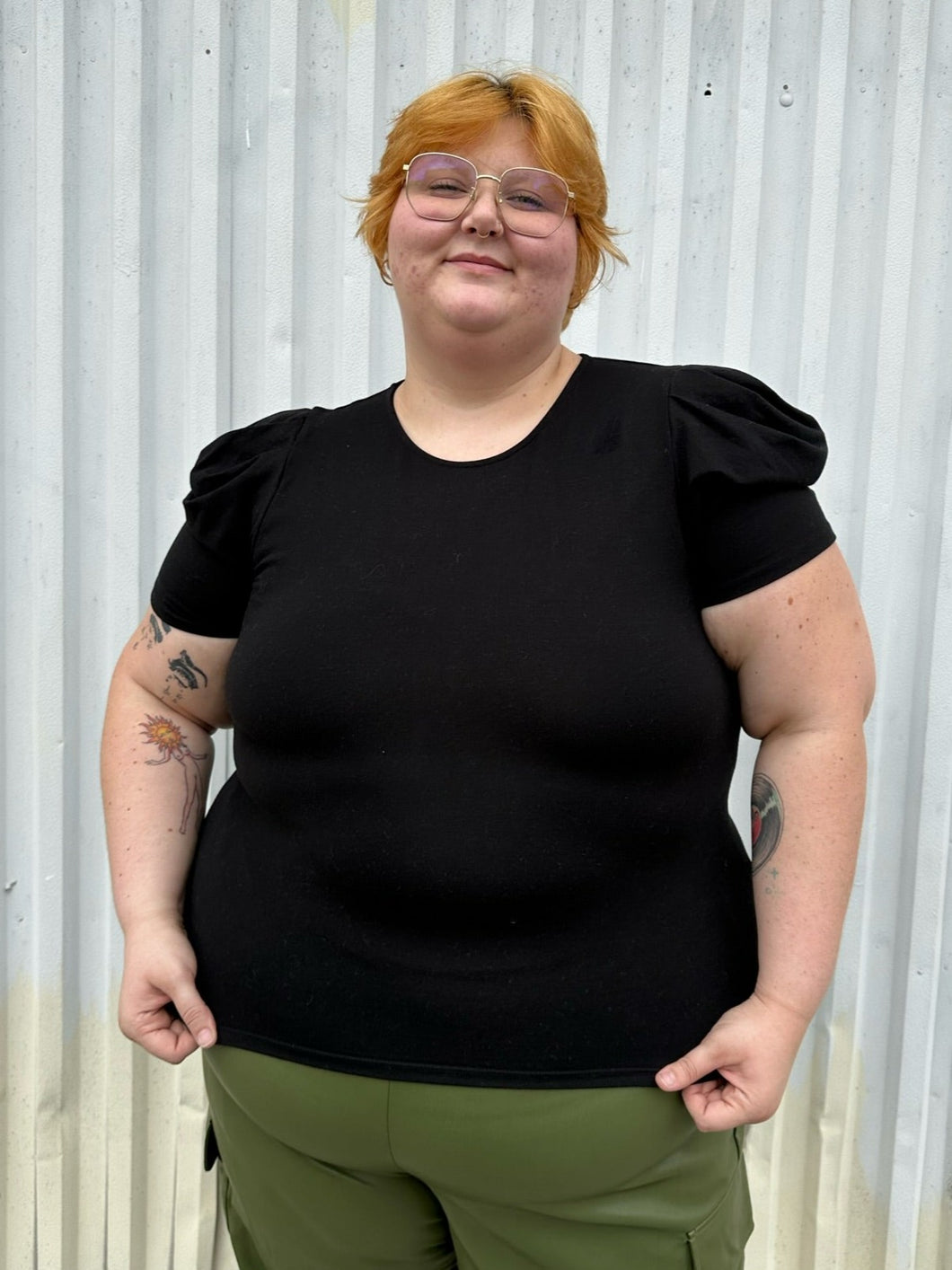 Front view of a size 3X Forever 21 black subtle puff sleeve t-shirt styled over green cargo pants on a size 22/24 model. The photo is taken outside in natural lighting.
