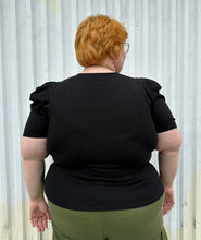 Load image into Gallery viewer, Back view of a size 3X Forever 21 black subtle puff sleeve t-shirt styled over green cargo pants on a size 22/24 model. The photo is taken outside in natural lighting.
