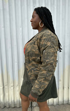 Load image into Gallery viewer, Side view of a size M (fits like 10/12) STAMPD brand camo zip-up bomber jacket styled open over a peach crop and green cargo skirt on a size 14/16 model. The photo is taken outside in natural lighting.
