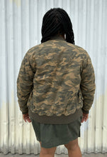 Load image into Gallery viewer, Back view of a size M (fits like 10/12) STAMPD brand camo zip-up bomber jacket styled open over a peach crop and green cargo skirt on a size 14/16 model. The photo is taken outside in natural lighting.
