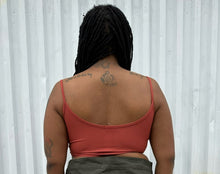 Load image into Gallery viewer, Back view of a size 12 Pretty Little Thing &quot;Second Skin&quot; rust-peach ribbed crop tank styled with an olive green cargo skirt on a size 14/16 model. The photo is taken outside in natural lighting.
