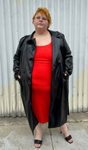 Load image into Gallery viewer, Full-body front view of a size 22/24 Eloquii black faux leather double-breasted long coat  with side slits, pockets, and cuffs styled open over a red dress on a size 22/24 model. The photo was taken outside in natural lighting.
