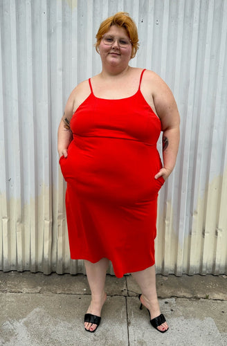 Full-body front view of a size 3X Amazon The Drop x Kellie B collab bright red tank dress with pockets styled with black kitten heels on a size 22/24 model. The photo was taken outside in natural lighting.