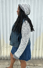 Load image into Gallery viewer, Side view of a size 1 Torrid medium wash denim jacket with hoodie sleeves and hood styled open and with the hood up over a rust-peach crop tank and denim skirt on a size 14/16 model. The photo is taken outside in natural lighting.
