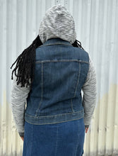Load image into Gallery viewer, Back view of a size 1 Torrid medium wash denim jacket with hoodie sleeves and hood styled open and with the hood up over a rust-peach crop tank and denim skirt on a size 14/16 model. The photo is taken outside in natural lighting.
