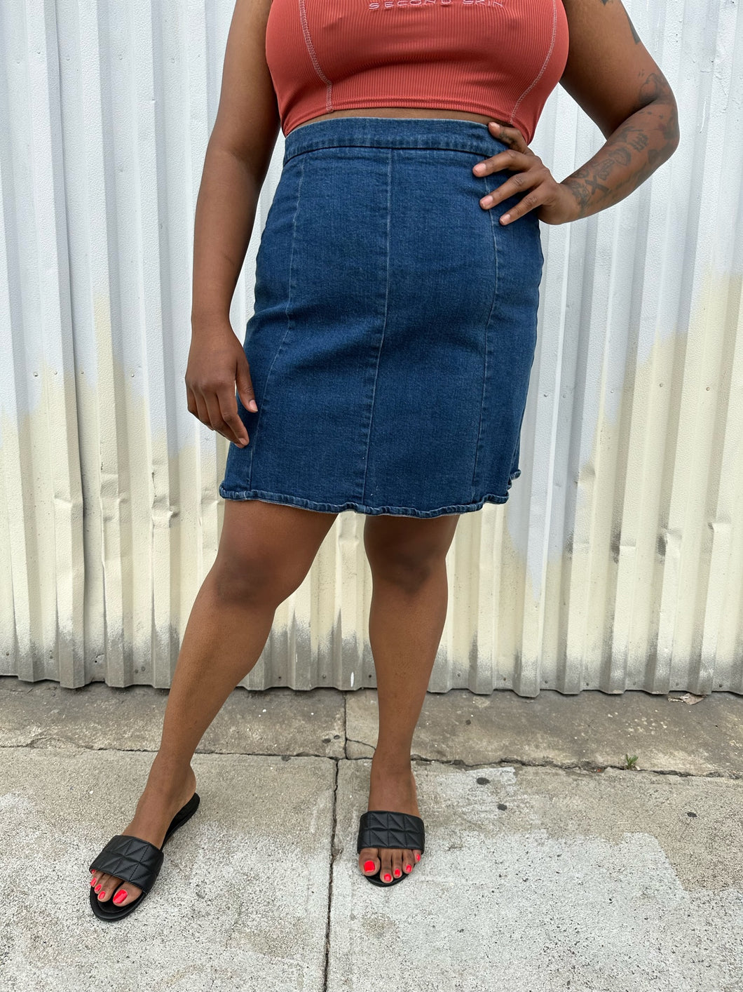 Front view of a size 16 ASOS medium wash denim pencil skirt styled with a rust-peach cropped tank and black flats on a size 14/16 model. The photo is taken outside in natural lighting.